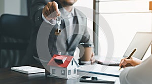 Home sales and home insurance concept. Estate agent giving house keys to woman and asked the customer to sign the documents to