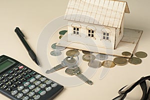 Home savings, budget concept. Model house, notepad, pen, calculator and coins on wooden office desk table.