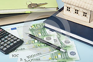 Home savings, budget concept. Model house, notepad, pen, calculator and coins on wooden office desk table.