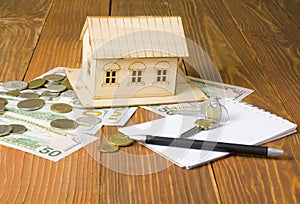 Home savings, budget concept. Model house, pen, keys notepad and money on wooden office desk table.