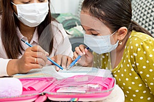 Home schooling concept image with mother and daughter studying while wearing face masks because of current corona virus threat