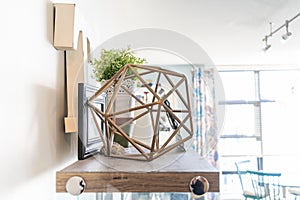 Home shelf with decorative knick knacks, including a geometric wire object, a letter `t`, picture frames and a planter. Bright liv