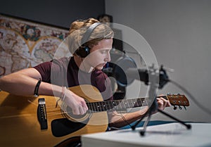 Home sound studio young teenager portrait playing guitar in Headphones and recording music using microphone. Modern audio