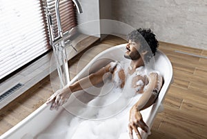 Home spa and relax on weekends. Relaxed indian man lying in bathtub with foam, enjoying bubble bath in morning