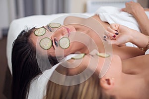 Home spa. Two women holding pieces of cucumber on their faces lying the bed.