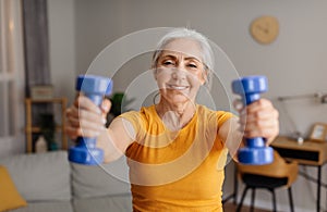 Home sports. Happy senior woman doing fitness exercises with weights, holding dumbbells and training at home