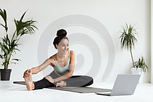 Home sports. Young beautiful woman training with laptop, stretching leg muscles