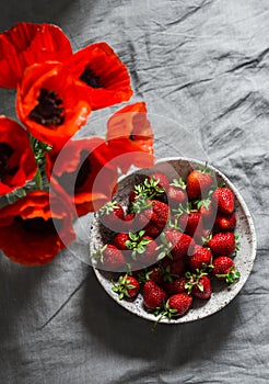 Home still life - ripe fresh strawberries in a bowl and a bouquet of red poppies on a gray background, top view