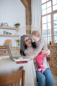 Stressed mom holding her daughter, kid interfering photo