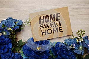 Home Sweet Home text message on paper card with flowers border frame on wooden background
