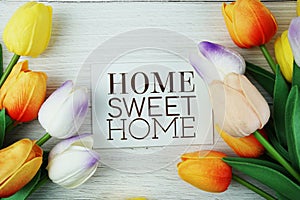 Home Sweet Home text message on paper card with tulip flowers bouquet top view on wooden background