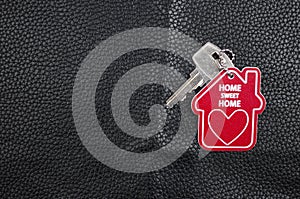 home sweet home written onto a red keyring, home shape over black leather background. Real estate concept for buying a new home