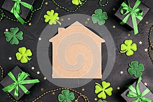 Home symbol surrounded by gifts, four-leaf clover and stars on black background. Copy space. St.Patrick`s day concept