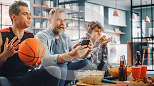 At Home Three Fans on Couch Watch Basketball Game on TV, Use Smartphone App for Checking Score