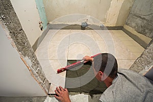 Home tiles improvement - handyman with level laying down tile floor. Renovation and construction concept.