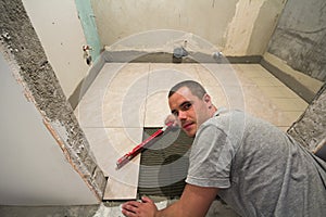 Home tiles improvement - handyman with level laying down tile floor. Renovation and construction concept.