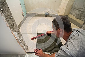 Home tiles improvement - handyman with level laying down tile floor. Renovation and construction concept.