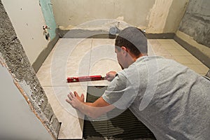 Home tiles improvement - handyman with level laying down tile floor. Renovation and construction concept.