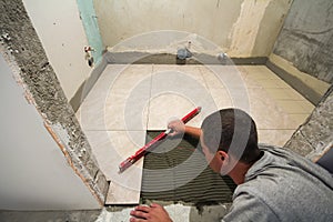 Home tiles improvement - handyman with level laying down tile floor. Renovation and construction concept.
