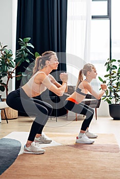 Home training. Mother and daughter doing squats