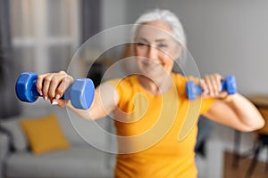 Home training on retirement. Fit senior woman doing exercises with dumbbells at home, working out her arm muscles