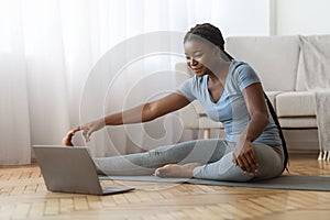 Home Training. Sporty african woman stretching leg muscles in front of laptop