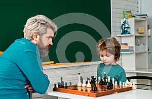 Home tutor helping boy with studies chess. Happy little kid playing chess with senior man at home.