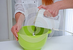 Home Ð¡ulinary Concept. Young woman baking a cake in the kitchen. Female using a handheld mixer to whisk the fresh ingredients in