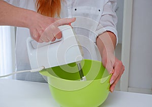 Home Ð¡ulinary Concept. Young woman baking a cake in the kitchen. Female using a handheld mixer to whisk the fresh ingredients in
