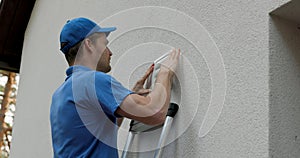 Home ventilation - hvac worker standing on ladder and installing air duct grille on house facade