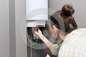 Home water heater, woman regulates the temperature on an electric water heater photo