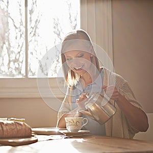 Home is where the tea is. A beautiful young woman pouring herself a cup of tea while sitting at table at home.