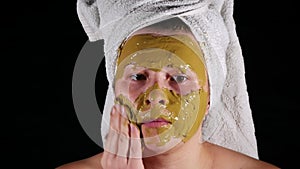 At home a woman with white towel on head applies a face mask out of clay.