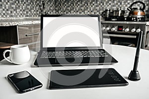 Home workplace of a graphic designer and architect in the kitchen. On the table is a laptop, graphics tablet and phone.