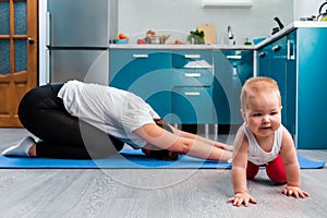 Home yoga. A young mother does a yoga asana on a mat. Her baby crawls around the mat. Sports and yoga at home with children