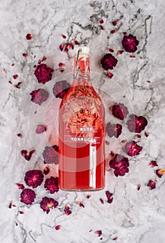 Homebrew rose Kombucha in swing top glass bottle with dried rose buds on white table background.