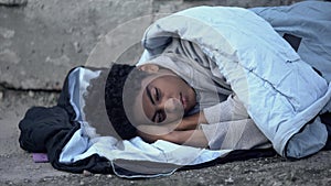 Homeless african teenager lying in sleeping bag ground, poverty unemployment