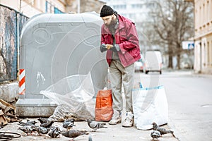 Homeless beggar feeding pigeons near the trash