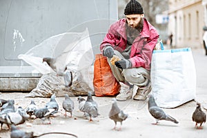 Homeless beggar feeding pigeons near the trash