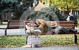 Homeless beggar man with a bag lying on bench outdoors in city, sleeping.