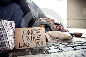 Homeless beggar man lying on the ground outdoors in city, sleeping.