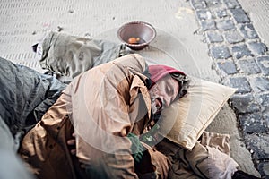 Homeless beggar man lying on the ground outdoors in city, sleeping.