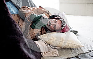 Homeless beggar man lying on the ground outdoors in city, warming up hands.