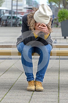 Homeless dejected woman sitting on a city bench