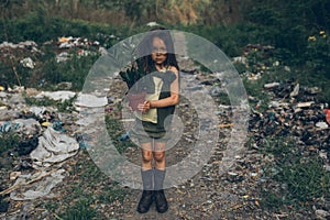 A homeless girl is standing on a garbage dump with a houseplant in a pot