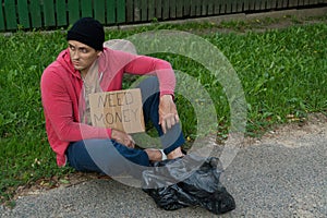 A homeless guy sits on the sidewalk with a cardboard and an inscription: need money