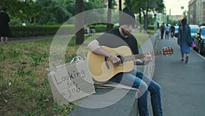 Homeless hungry man on the street playing guitar, looking for a job