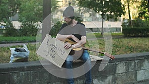 Homeless hungry man on the street sitting on parapet, looking for a job