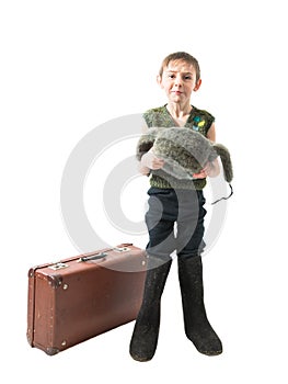 Homeless little boy standing in felt boots next to a suitcase and begs for alms holding in hands hat