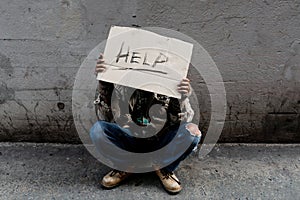 A homeless, long-haired Asian man sits hopelessly leaning against a wall as there is no one to help him with work and food in his